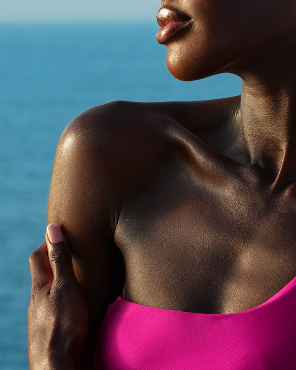 A dark-skin model applying beauty balm on her shoulder on the ocean background