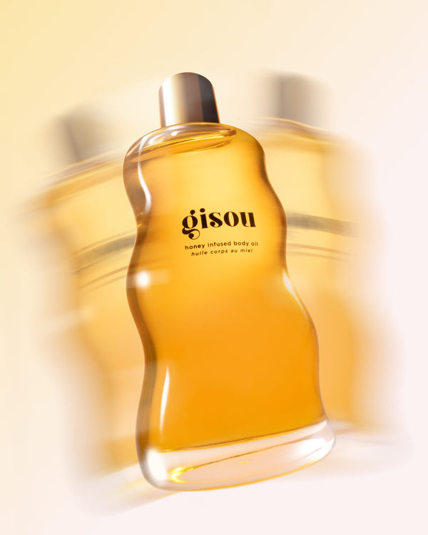 A bottle of the honey infused body oil shaking on the white background